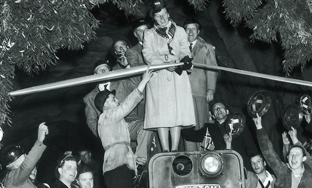 Archival black-and-white photograph of Mrs Eileen Hudson cutting a ribbon at the opening of the Guthega Tunnel in 1954, with workers and attendees around her.