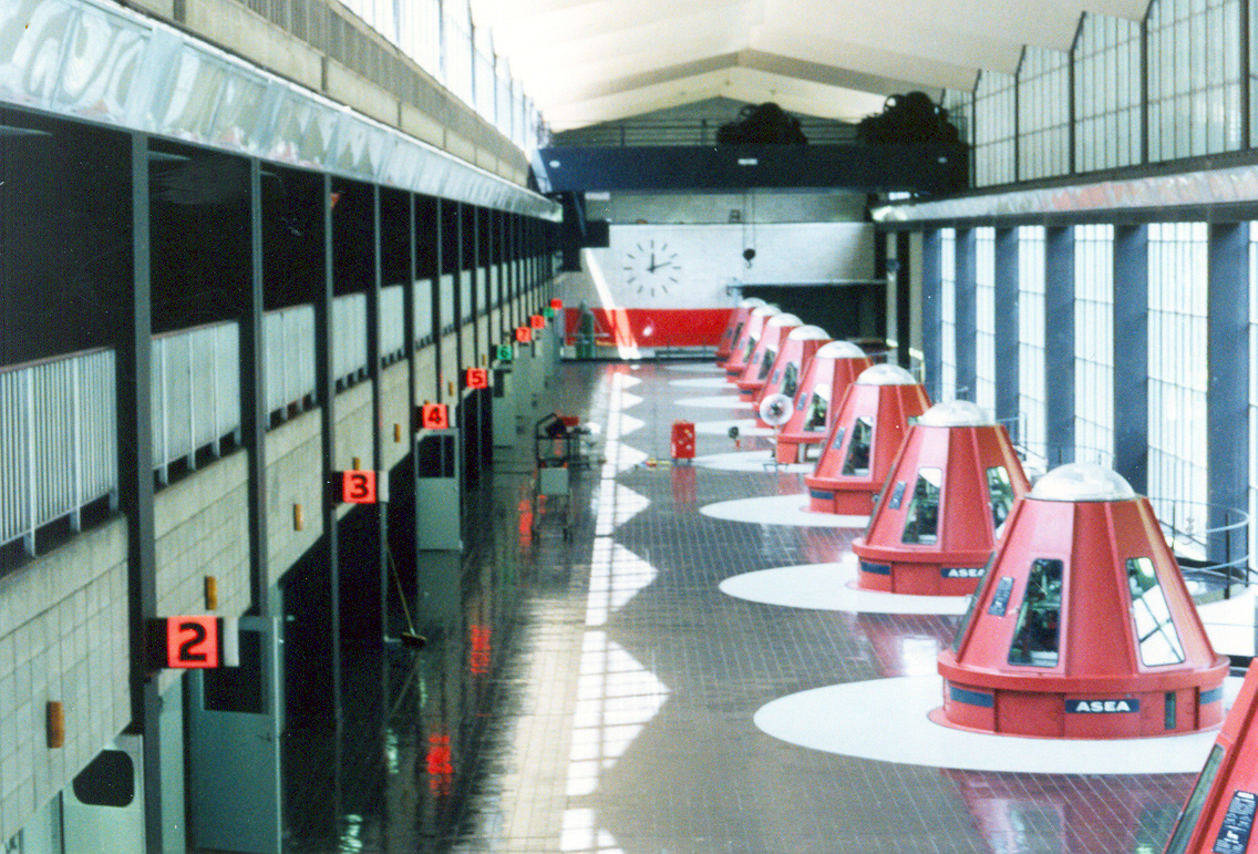 Interior of Tumut 1 Power Station, showing a row of red generator housings in a long hall.
